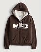 Женская меховая толстовка на молнии и с капюшоном Hollister коричневого цвета с белой нашитой надписью. Модель 06531. Подробное описание и цена товара. Доставка по России, Москве и Области от Moscow USA